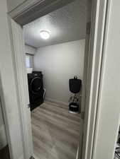 Laundry area with washer / clothes dryer, light hardwood / wood-style floors, and a textured ceiling