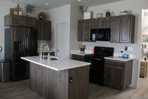 Kitchen with dark brown cabinets, sink, a center island with sink, and black appliances