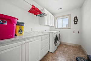 Laundry room featuring separate washer and dryer, light tile patterned floors, and cabinets