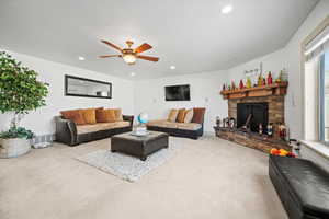 Carpeted living room featuring ceiling fan and a stone fireplace