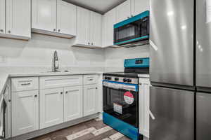 Kitchen with sink, stainless steel appliances, white cabinets, and light stone countertops