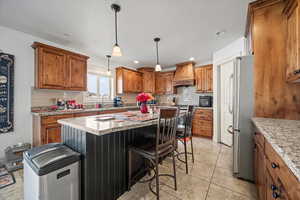 Kitchen featuring a kitchen island, hanging light fixtures, stainless steel appliances, light stone countertops, and custom range hood