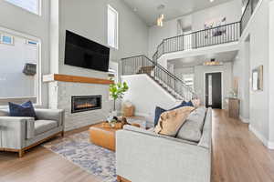 Living room with a towering ceiling, a stone fireplace, and light wood-type flooring