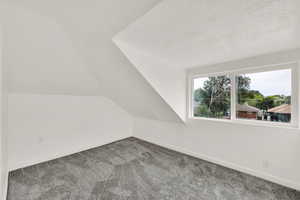 Upstairs bedroom with lofted ceiling, carpet flooring, and a textured ceiling