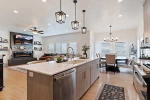 Kitchen with appliances with stainless steel finishes, decorative light fixtures, sink, a large fireplace, and a center island with sink