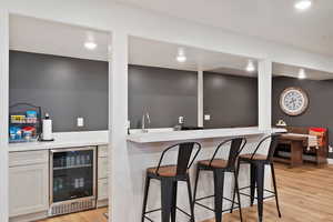 Kitchenette featuring white cabinets, sink, beverage cooler, and light hardwood / wood-style floors