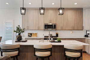 Kitchen with a breakfast bar, a center island with sink, light brown cabinetry, and decorative light fixtures