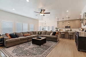 Living room featuring ceiling fan with notable chandelier, light hardwood / wood-style flooring, and a textured ceiling