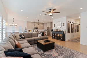 Living room with ceiling fan with notable chandelier and light hardwood / wood-style flooring