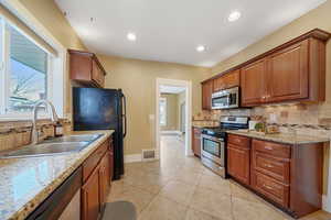 Kitchen featuring stainless steel appliances, light tile patterned flooring, light stone countertops, and sink