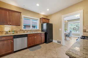 Kitchen featuring sink, tasteful backsplash, light stone countertops, black fridge, and stainless steel dishwasher