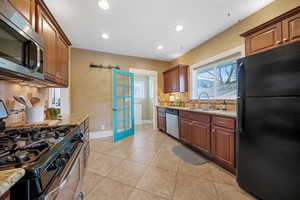 Kitchen with stainless steel appliances, light stone countertops, sink, and backsplash