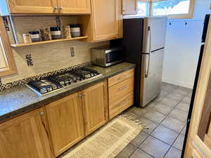 Kitchen featuring light tile patterned floors, decorative backsplash, and appliances with stainless steel finishes