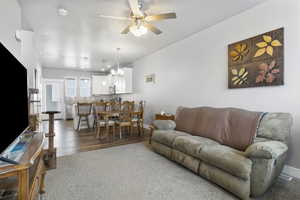 Living room featuring ceiling fan with notable chandelier and LVP / wood-style flooring