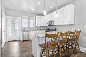 Kitchen with pendant lighting, a breakfast bar area, appliances with stainless steel finishes, white cabinetry, and kitchen peninsula