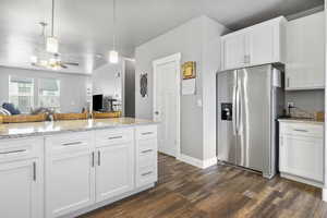 Kitchen featuring white cabinetry, dark LVP / wood-style floors, stainless steel refrigerator with ice dispenser, light stone counters, and decorative light fixtures