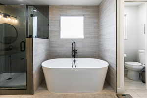 Bathroom featuring toilet, separate shower and tub, and tile walls