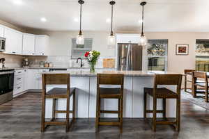 Kitchen featuring appliances with stainless steel finishes, pendant lighting, white cabinets, a kitchen breakfast bar, and a center island