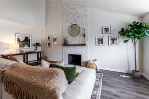 Living room featuring a stone fireplace, dark wood-type flooring, a textured ceiling, and high vaulted ceiling