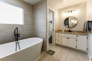 Bathroom with vanity, a tub to relax in, tile walls, and toilet