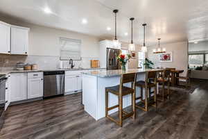 Kitchen with white cabinetry, appliances with stainless steel finishes, a center island, and hanging light fixtures