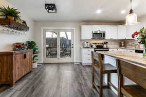 Kitchen with pendant lighting, appliances with stainless steel finishes, light stone countertops, white cabinets, and dark hardwood / wood-style flooring