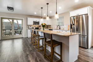 Kitchen featuring stainless steel appliances, white cabinetry, a kitchen island, and hanging light fixtures