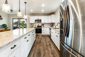 Kitchen with appliances with stainless steel finishes, sink, white cabinets, hanging light fixtures, and light stone counters