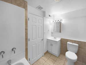 Bathroom with a bathing tub, tile walls, tile patterned flooring, vanity, and toilet