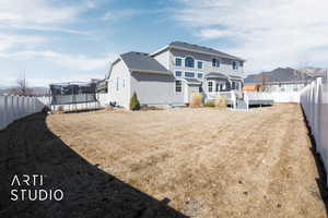 Rear view of house featuring a deck, a trampoline, a fenced backyard, and a residential view