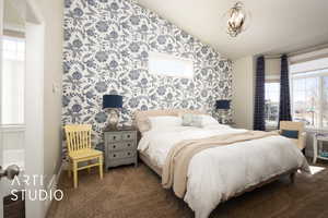 Bedroom featuring lofted ceiling, dark carpet, an inviting chandelier, and wallpapered walls