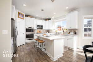 Kitchen with a center island, dark wood-style flooring, stainless steel appliances, hanging light fixtures, and white cabinetry