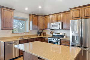 Kitchen featuring tasteful backsplash, appliances with stainless steel finishes, light stone countertops, and sink