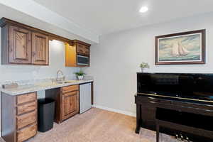 Kitchen featuring stainless steel microwave, dishwasher, sink, light colored carpet, and light stone counters