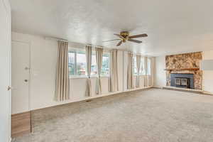 Unfurnished living room with ceiling fan, a stone fireplace, carpet, and a textured ceiling