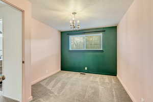 Carpeted spare room with a textured ceiling and an inviting chandelier