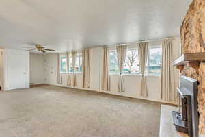 Unfurnished living room with a wood stove, light colored carpet, and ceiling fan