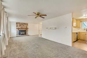 Unfurnished living room with ceiling fan, light colored carpet, a fireplace, and sink