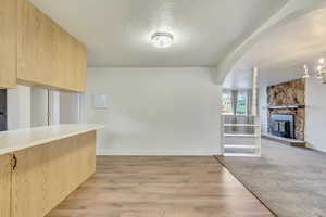 Kitchen with a fireplace, light wood-type flooring, a chandelier, light brown cabinets, and a textured ceiling