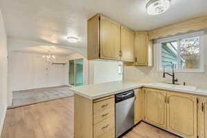 Kitchen with sink, light hardwood / wood-style floors, stainless steel dishwasher, kitchen peninsula, and light brown cabinets