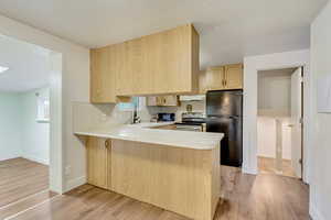 Kitchen featuring light brown cabinetry, black appliances, kitchen peninsula, and light wood-type flooring