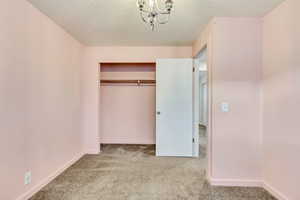 Unfurnished bedroom with a notable chandelier, light colored carpet, a closet, and a textured ceiling