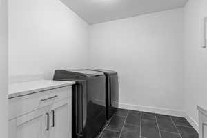 Clothes washing area featuring cabinets, separate washer and dryer, and dark tile patterned flooring