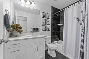 Full bathroom featuring tile patterned flooring, vanity, toilet, shower / bath combo, and a textured ceiling