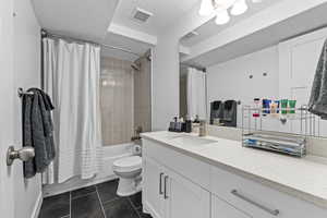 Full bathroom featuring vanity, shower / tub combo, toilet, tile patterned floors, and a textured ceiling