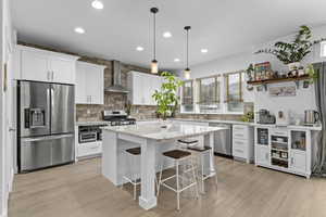 Kitchen featuring wall chimney exhaust hood, a breakfast bar, appliances with stainless steel finishes, a kitchen island, and white cabinets