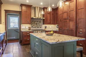 Kitchen featuring a center island, pendant lighting, wall chimney range hood, light stone countertops, and a baseboard heating unit