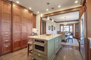 Kitchen featuring stainless steel appliances, light stone counters, wood-type flooring, a kitchen island, and decorative light fixtures