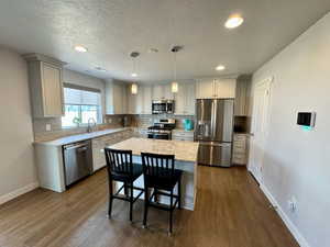 Kitchen featuring pendant lighting, appliances with stainless steel finishes, backsplash, a kitchen island, and dark hardwood / wood-style flooring