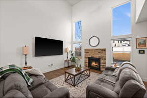 Living room with a high ceiling, a stone fireplace, and hardwood / wood-style floors